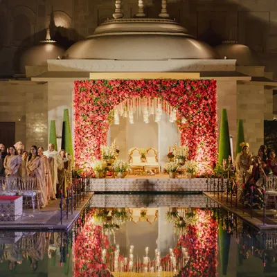 A mandap that appears to float on water. For this wedding at Fairmont Jaipur, we created a breathtaking floral arch reflected perfectly in the still water, surrounded by candles to create a surreal, romantic atmosphere for the ceremony.