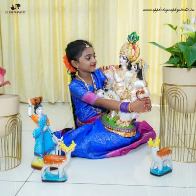 A young girl poses with a Krishna statue during a festive studio shoot. We provide props and backdrops to create an authentic and celebratory atmosphere for these special portraits.