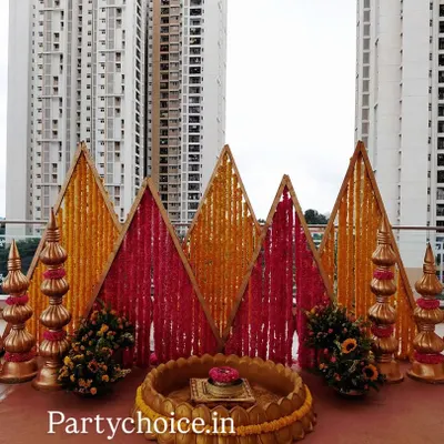 A striking backdrop for a Haldi or Harishinashasthra ceremony. The design uses geometric panels of yellow and pink marigolds, flanked by traditional golden props.