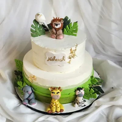 A fun and friendly jungle theme cake. This two-tier cake is filled with gems, kisses, and jellies for a surprise inside. It's decorated with cute, handcrafted fondant animals like a lion, giraffe, and elephant.
