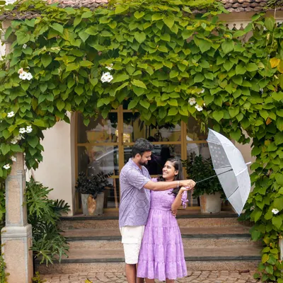 A sweet, playful moment during a pre-wedding shoot in Pondicherry, using a simple umbrella prop against a lush, green backdrop.