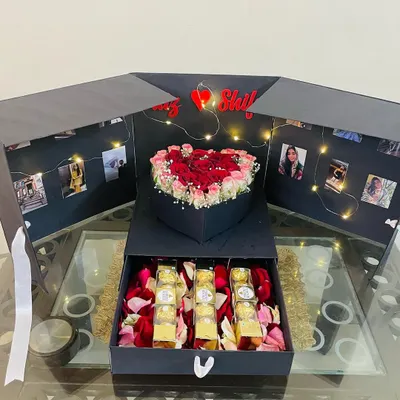 The complete view of our surprise explosion box, open to display the central heart-shaped rose arrangement, photo-lined walls with fairy lights, and a drawer of chocolates. It's a truly immersive and personal gift.