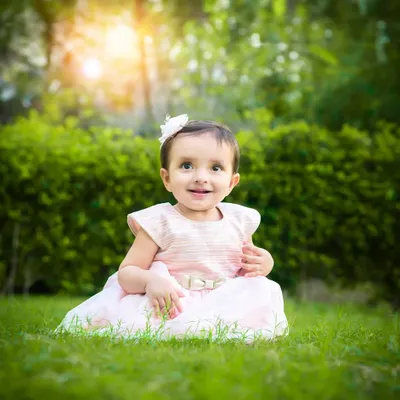 A baby girl sits in a lush green park, the sunlight creating a beautiful halo effect around her. A perfect example of a magical outdoor portrait.