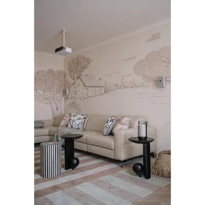A full view of the den and media lounge, showing the hand-painted mural that wraps around the room. The custom black side tables add a strong, graphic element to the soft space.