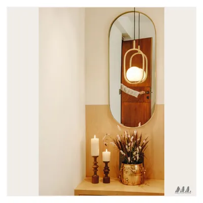 A simple yet elegant corner vignette. The composition of a modern pendant light, an oval mirror, and classic candle holders creates a warm and welcoming ambiance.