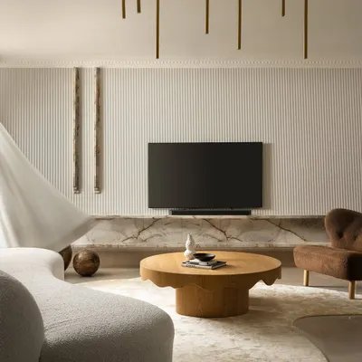 A glimpse into the living area of Ecru House, where a fluted wall texture, an organically shaped rug, and a sculptural brass chandelier come together. This composition highlights our focus on warm minimalism and creating visual rhythm through texture and form.