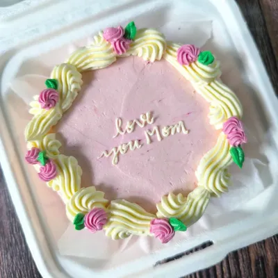 A beautiful and classic bento cake for Mom. This design features a wreath of piped buttercream roses and leaves surrounding a heartfelt message in delicate script.