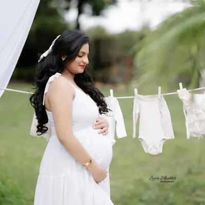 A sweet and symbolic outdoor shot. The line of baby clothes hanging in the background is a lovely touch that speaks of the joyful preparations for the new arrival.