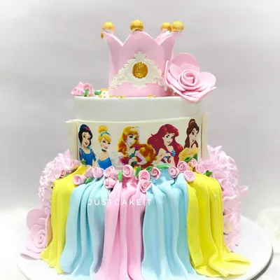 A grand three-tiered Disney princess cake featuring edible images of the princesses and beautiful fondant drapery. The design is topped with a handcrafted crown, making it fit for royalty.