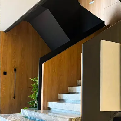 This modern staircase is a statement of minimalist architecture. Crafted from sleek black metal, warm wood paneling, and solid marble steps, the design balances elegance and functionality, creating a sculptural transition between floors.