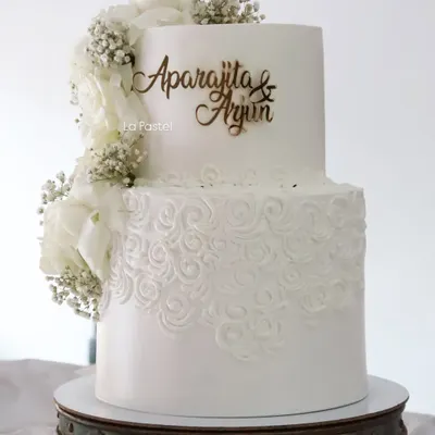 An all-white, two-tier beauty. The bottom tier features a delicate hand-piped rosette pattern, while a cascade of white wafer paper flowers and baby's breath adds a touch of modern romance.