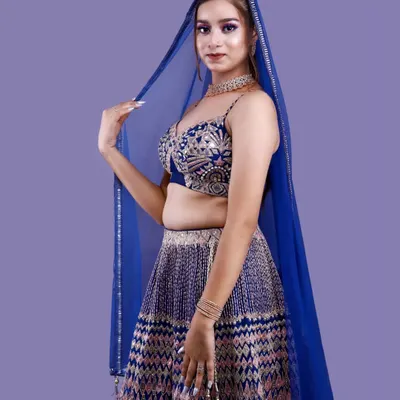 A striking studio portrait against a solid lavender background. The model's royal blue lehenga and sheer dupatta are the focus, demonstrating our skill in capturing traditional wear with a modern, editorial feel.