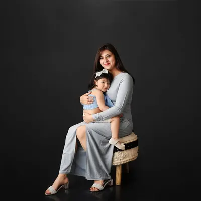 A simple and elegant mother-daughter portrait against a dark background. The coordinating blue outfits and their gentle embrace create a sweet and timeless image.