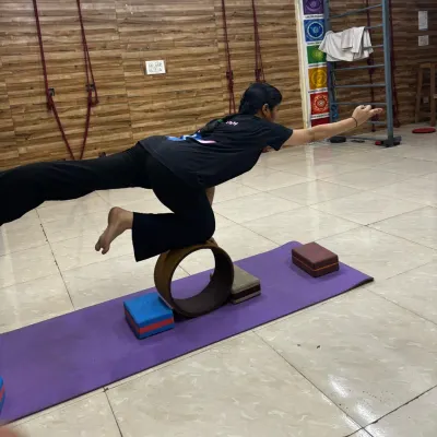A student practices Virabhadrasana III (Warrior III) on a yoga wheel, a powerful pose for building full-body stability.