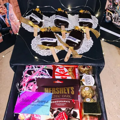 The top layer of this surprise box reveals custom-made chocolate cakesicles with anniversary wishes. Below, a drawer is filled with an assortment of chocolates like Hershey's, KitKat, and Ferrero Rocher.