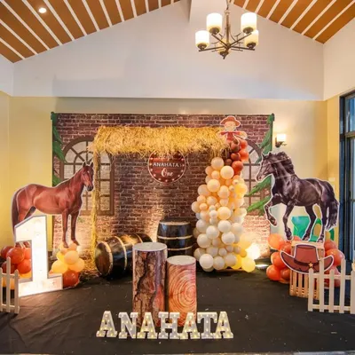 A rustic barnyard theme for Anahata's first birthday. We used a brick wall backdrop, hay bales, horse cutouts, and wooden barrels to create an authentic rodeo feel.