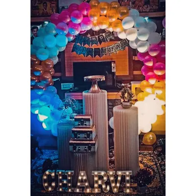 A vibrant and colorful birthday setup featuring a rainbow balloon arch and the name 'CHARVI' in light-up letters. This fun and cheerful decoration is perfect for adding a splash of color to any party.
