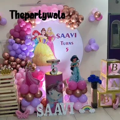 A grand princess party for Saavi's 5th birthday, featuring a backdrop with multiple Disney princesses. The purple, pink, and rose gold balloons, along with light-up "BABY" boxes, create a royal atmosphere.