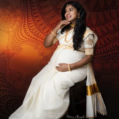 The timeless beauty of a white and gold Kasavu saree. This mom-to-be looks absolutely radiant in this traditional attire against an artistic backdrop.