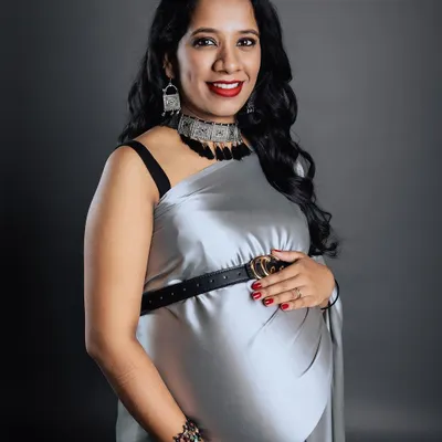 A stunning studio portrait of a mother-to-be, radiating confidence in a modern silver saree styled with a belt. This image showcases a chic and contemporary approach to maternity fashion.