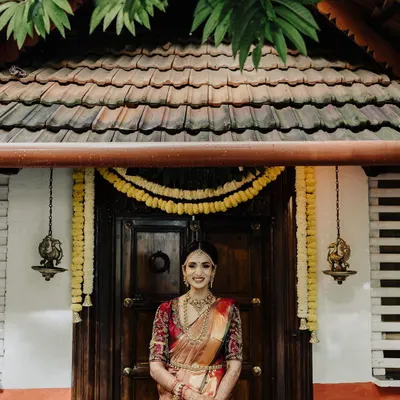 A beautiful full-length bridal portrait in front of a traditional wooden door. The symmetry and rich textures of the background perfectly complement the bride's elegant Kanjeevaram saree and jewelry.
