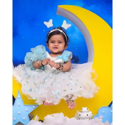 A sweet smile from a 'Moon & Stars' themed session. This little girl is dressed in a beautiful ruffled dress, sitting on a large crescent moon prop against a starry night sky backdrop.