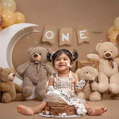 This little girl is all smiles during her teddy bear-themed first birthday cake smash. We designed this cozy, neutral-toned setup with a crescent moon, balloons, and lots of cuddly friends for her special milestone.