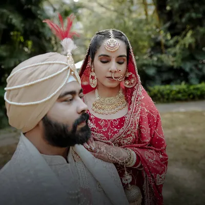 An artistic portrait of a Punjabi bride and groom. The bride, in her stunning red lehenga, rests her hand on the groom's shoulder, creating a regal and timeless image.