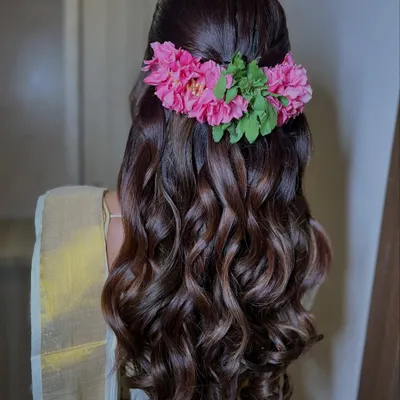 A beautiful half-up, half-down hairstyle with soft waves, adorned with a vibrant pink floral accessory for a South Indian bride.