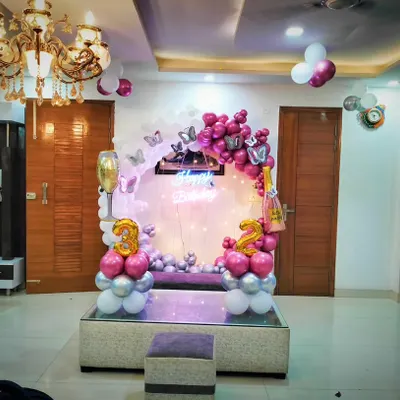 A sophisticated 32nd birthday decoration at home. The setup includes a circular backdrop with pink and silver balloons, butterfly accents, and large number foil balloons, all elegantly arranged around a glass table.