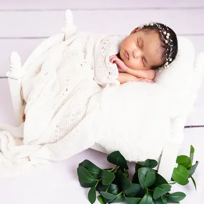 A perfect, peaceful newborn sleeping on a tiny white bed prop, swaddled in a soft white blanket. An angelic and timeless portrait.