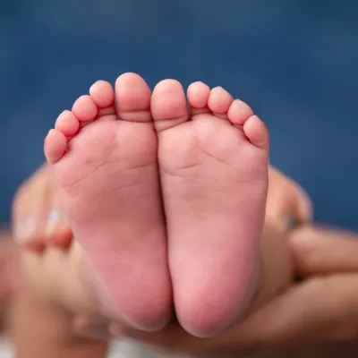 A macro shot focusing on the perfect, tiny soles of a newborn's feet, held gently in their parent's hands. These are the details that change in a blink, and we make sure to capture them for you to cherish forever.