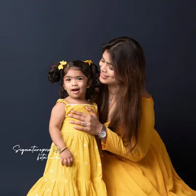 A beautiful moment of connection between a mother and her daughter. Dressed in coordinating yellow outfits, their shared smile is the focus of this simple and elegant studio portrait.