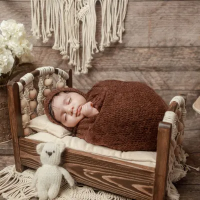 A baby swaddled in a warm brown wrap, sleeping peacefully on a rustic wooden bed with macrame details. This setup showcases our love for natural textures and tones.
