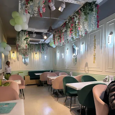 The interior of a restaurant in GK 1, featuring a pastel color scheme with pink and green chairs. I used wall molding and floral ceiling installations to create a whimsical and charming dining atmosphere.