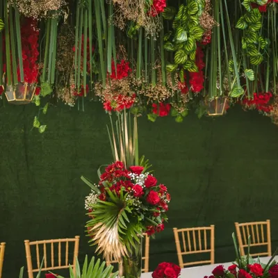 A tablescape that is a work of art. We designed this setting with a dramatic overhead installation of hanging red flowers and greenery, complemented by lush red floral centerpieces on the table below.