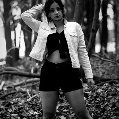 A powerful black and white portrait in a forest setting. The monochrome tones emphasize the texture of the leaves and the subject's confident stance.