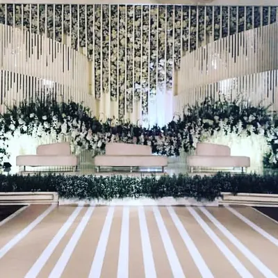 A modern and sophisticated reception stage design featuring clean lines and a neutral color palette. The backdrop uses white floral arrangements and textured panels to create a chic, minimalist look for a contemporary wedding.