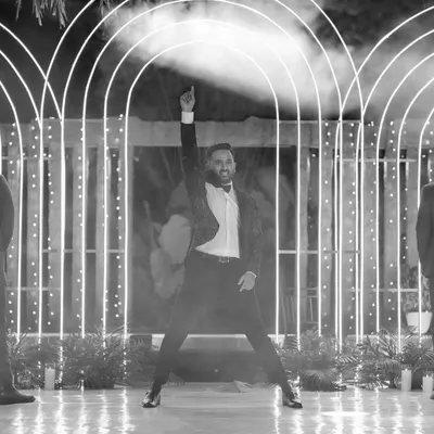A groom strikes a pose in a black-and-white shot, part of a larger performance telling the couple's love story.