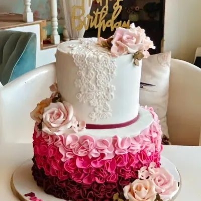 A stunning two-tier cake with a dramatic pink and burgundy ombre ruffle effect on the bottom tier and delicate lace piping on top.