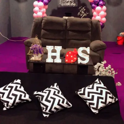 A cozy birthday setup perfect for a couple or a few friends. This room features a pink and purple balloon arch, a comfortable recliner, and custom initial lights, creating an intimate space for your private birthday movie screening.