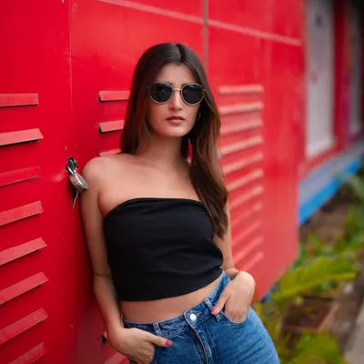 A classic street style portrait. The model's simple black tube top and jeans pop against the vibrant red industrial background, creating a look that is both cool and confident.