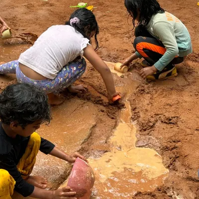 Children work together to dig channels and create rivers in the mud pit on a rainy day. This is collaborative, sensory play at its best.