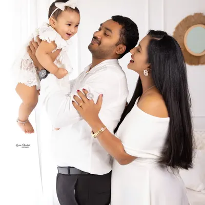 A picture-perfect family moment. The joy is contagious as this mom and dad lift their laughing baby girl, all dressed in coordinating white outfits.