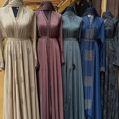 A beautiful selection of modest abayas on display, showcasing a variety of colours from beige and mauve to teal and navy. Each features unique detailing, perfect for finding a style that suits you.