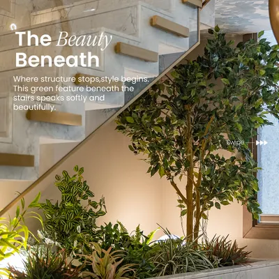 A lush arrangement of faux greenery and a statement tree fills the space under a modern staircase. This design uses backlighting to create depth and highlight the varied leaf shapes, turning dead space into a beautiful feature.