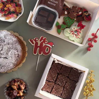 My Christmas goodie box is filled with holiday magic. It contains a variety of festive treats, including hand-decorated sugar cookies, a Belgian chocolate brownie, and a macaron wreath.