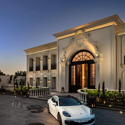 The Grand Alabaster residence at dusk, where architectural lighting accentuates its neoclassical details. The arched entrance and symmetrical facade create an imposing yet elegant presence, a hallmark of our classical designs.