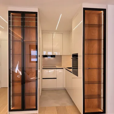 A wider view of this modern kitchen, showing how the two tall, illuminated display cabinets frame the space. The warm wood interior contrasts beautifully with the high-gloss white cabinetry.