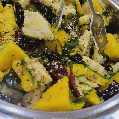 A close-up of our soft and spongy Khaman Dhokla, a classic Gujarati snack. It's tempered with mustard seeds and curry leaves, showcasing our commitment to authentic flavors.